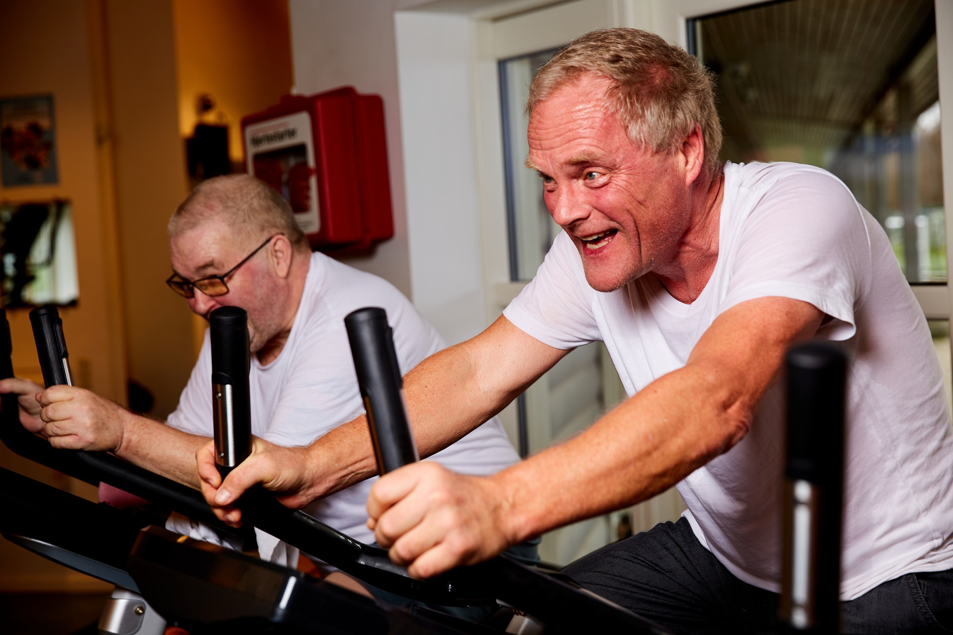To ældre herrer knokler på motionscykler