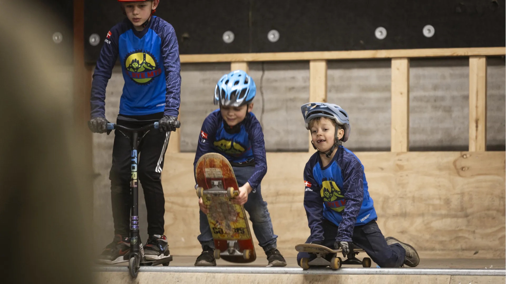 Tre børn kører på løbehjul og skateboard på en rampe i Kostalden i foreningen Gl. Rye MTB.