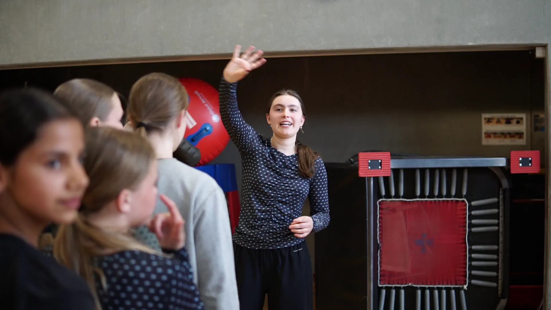 Mathilde i fuld gang med at instruere – hendes armbevægelser viser næste øvelse, mens gymnasterne følger med og spejler hendes bevægelser.